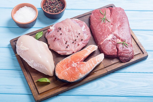 Selection of animal-based foods allowed on the carnivore diet, including raw chicken, pork, salmon, and beef, displayed on a wooden cutting board