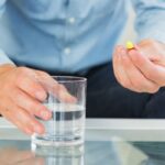 Man holding stimulant laxative capsule and glass of water, representing fast-acting constipation relief options.