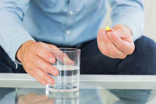 Man holding stimulant laxative capsule and glass of water, representing fast-acting constipation relief options.