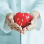 Female medical doctor holding red heart shape in hand with graphic of heart beat, cardiology and insurance concept