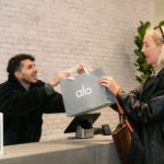 Woman exiting Alo Yoga store at Fashion Island in Newport Beach, California with shopping bag, showcasing in-store purchase experience for Alo activewear.