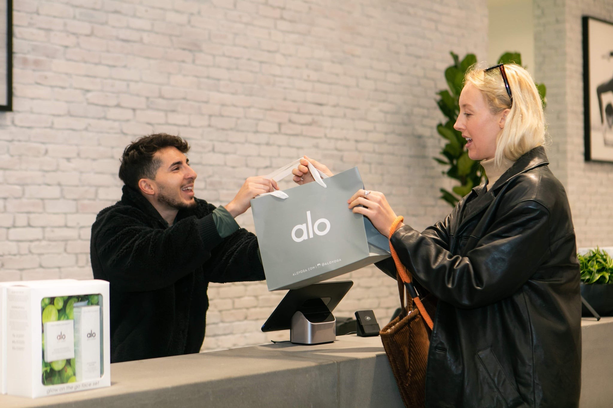 Woman exiting Alo Yoga store at Fashion Island in Newport Beach, California with shopping bag, showcasing in-store purchase experience for Alo activewear.