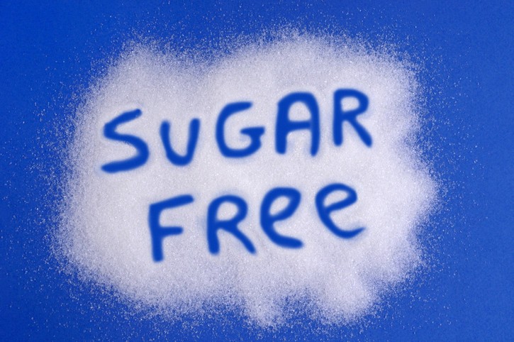 A blue background sprinkled with white sugar substitute crystals with the words sugar free written; concept is sugar alcohols and artificial sweeteners