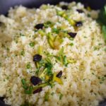 Couscous in a black dish with dried cherries and pistachios on top