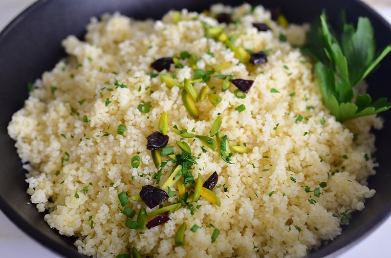 Couscous in a black dish with dried cherries and pistachios on top