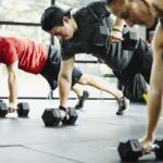 Three men perform modified push-up exercises with dumbbells, highlighting creatine's benefits for strength training in a gym setting.