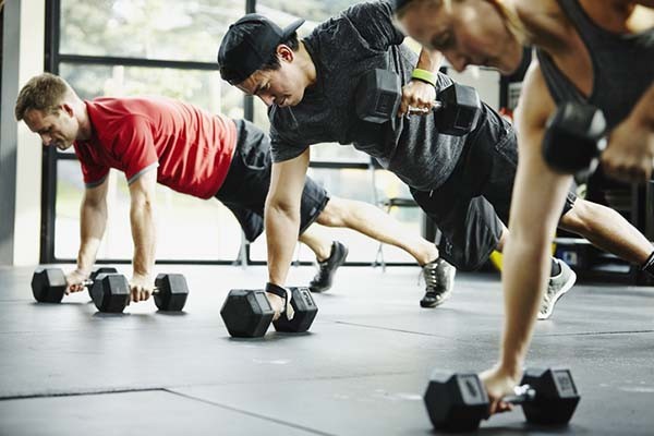 Three men perform modified push-up exercises with dumbbells, highlighting creatine's benefits for strength training in a gym setting.