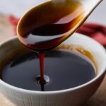 Close-up of eel sauce being drizzled from a spoon, highlighting its thick and glossy texture.