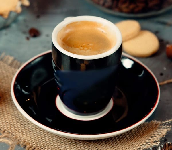 A cup of Americano surrounded by coffee beans and espresso grounds, highlighting the simple yet flavorful ingredients of this coffee beverage.