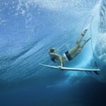 Female Pro surfer dives through the water with her board at Cloud Break Fiji