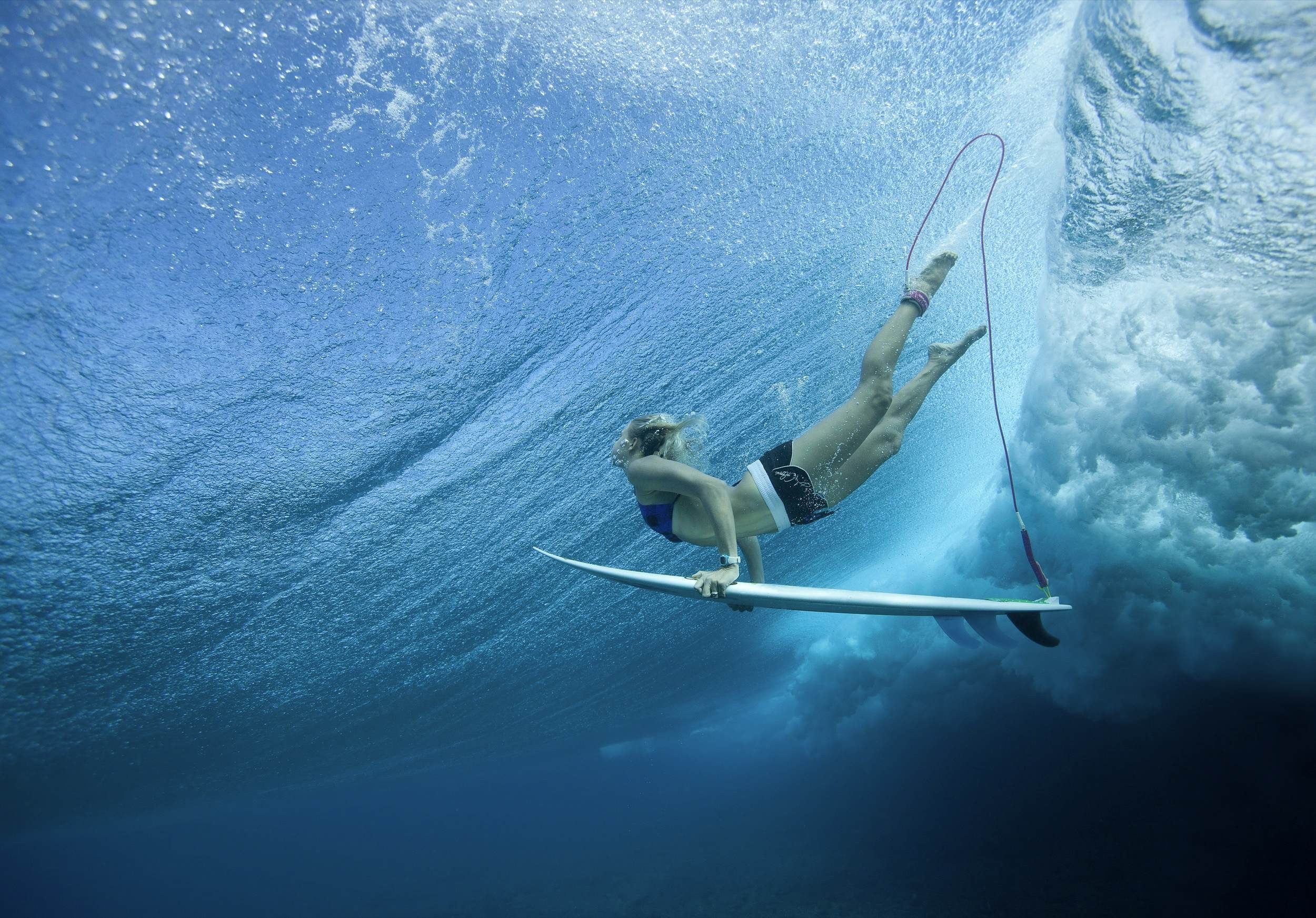 Female Pro surfer dives through the water with her board at Cloud Break Fiji