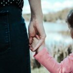 A parent gently holds their child's hand, symbolizing the supportive and healthy relationship that contrasts with the controlling nature of an 'almond mom' parenting style which can negatively impact a child's relationship with food and body image.