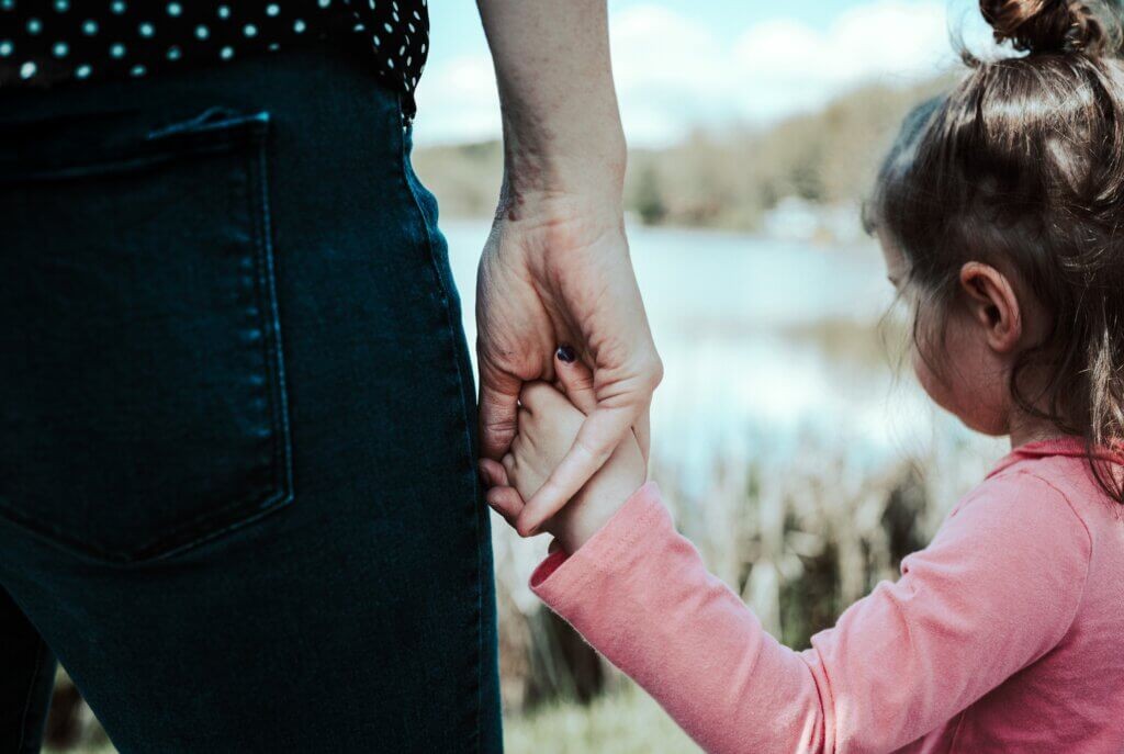 A parent gently holds their child's hand, symbolizing the supportive and healthy relationship that contrasts with the controlling nature of an 'almond mom' parenting style which can negatively impact a child's relationship with food and body image.