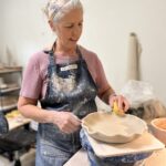 Close-up shot of Beth Smith's hands shaping clay on a pottery wheel in her studio.