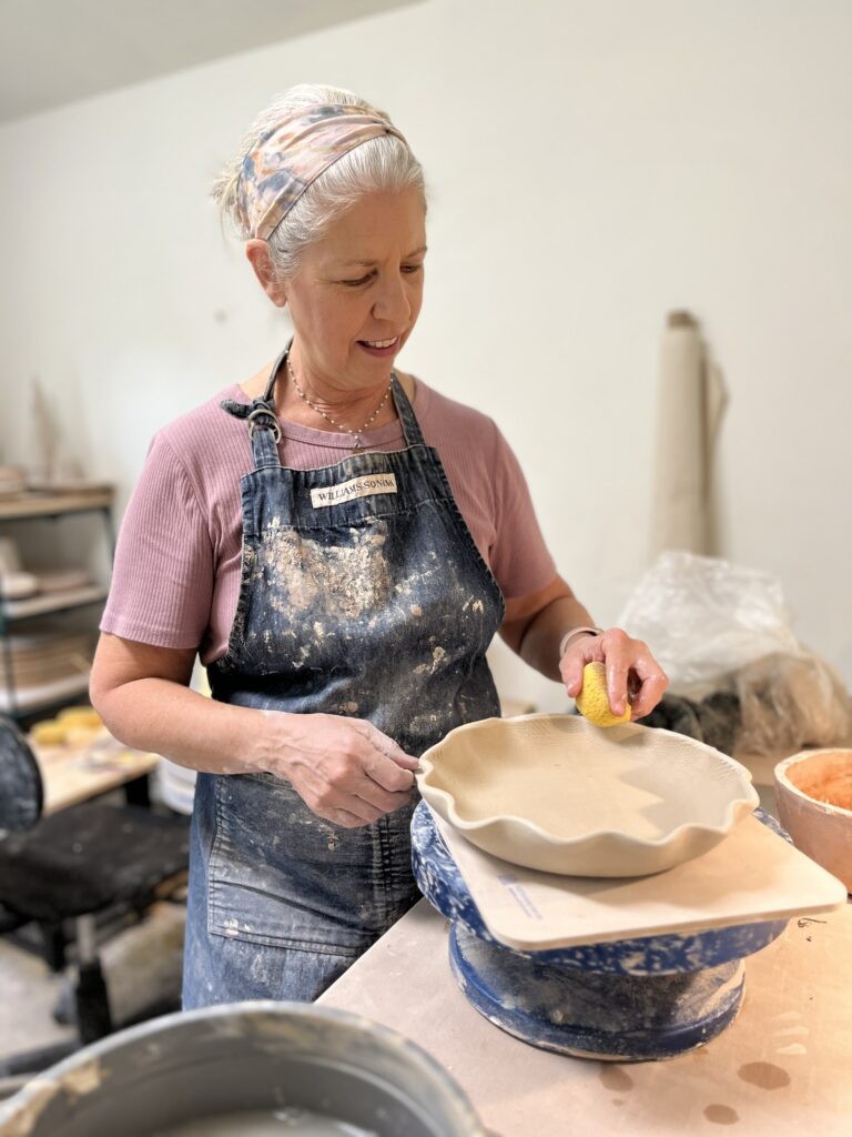 Close-up shot of Beth Smith's hands shaping clay on a pottery wheel in her studio.