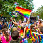 A mixed group of revelers including adults and children dressed in rainbow colors celebrate Pride Festival in Dublin in June, flying flags and blowing bubbles