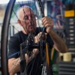 An older man with glasses works on repairing a bicycle wheel.