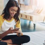 Young woman sitting on the floor with her phone learning German