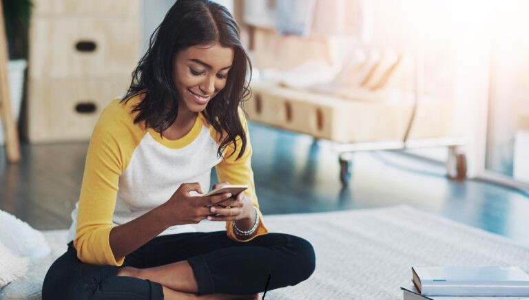 Young woman sitting on the floor with her phone learning German