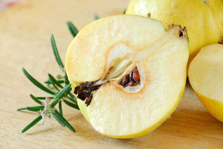 Quince cut in half with seeds next to a sprig of rosemary