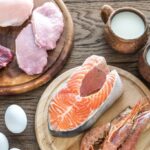 Variety of vitamin B12 rich foods including beef steak, salmon, eggs, milk, cheese, and shellfish, showcasing natural dietary sources of cobalamin.