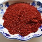 Close-up of vibrant red sumac spice in a small blue and white patterned dish, showcasing its texture and color.