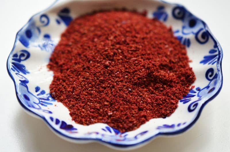 Close-up of vibrant red sumac spice in a small blue and white patterned dish, showcasing its texture and color.