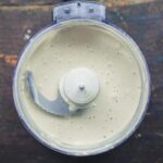 Tahini sauce being blended in a food processor, showcasing the emulsification process and transformation into a smooth sauce.