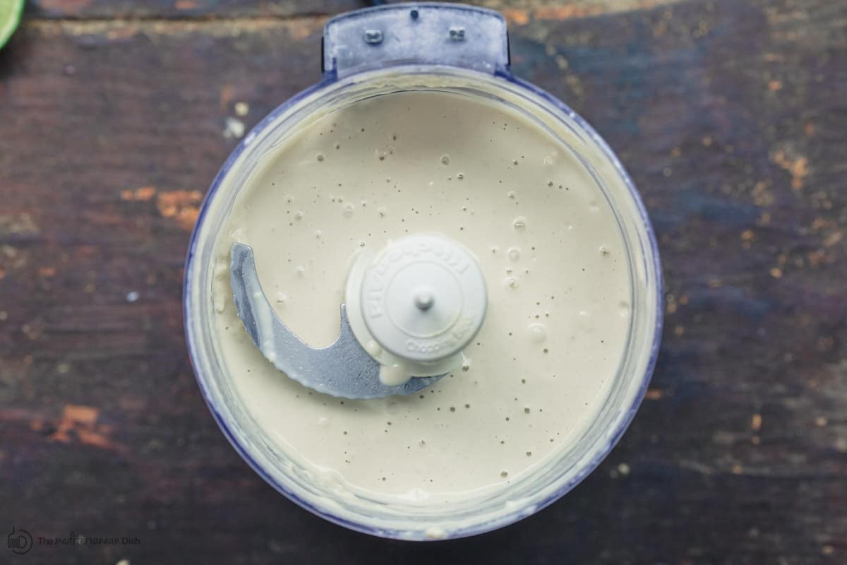 Tahini sauce being blended in a food processor, showcasing the emulsification process and transformation into a smooth sauce.