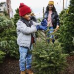 Young boy in a red jacket holding a small Christmas tree at a Christmas tree lot