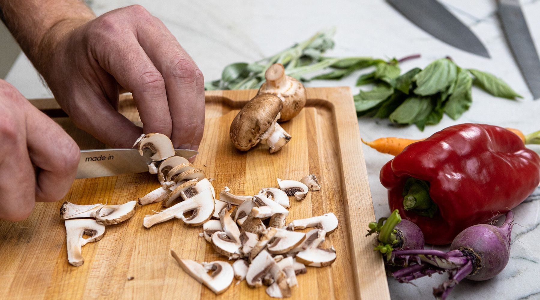 Hands holding a paring knife and cutting vegetables on a wooden cutting board, demonstrating proper knife handling technique.