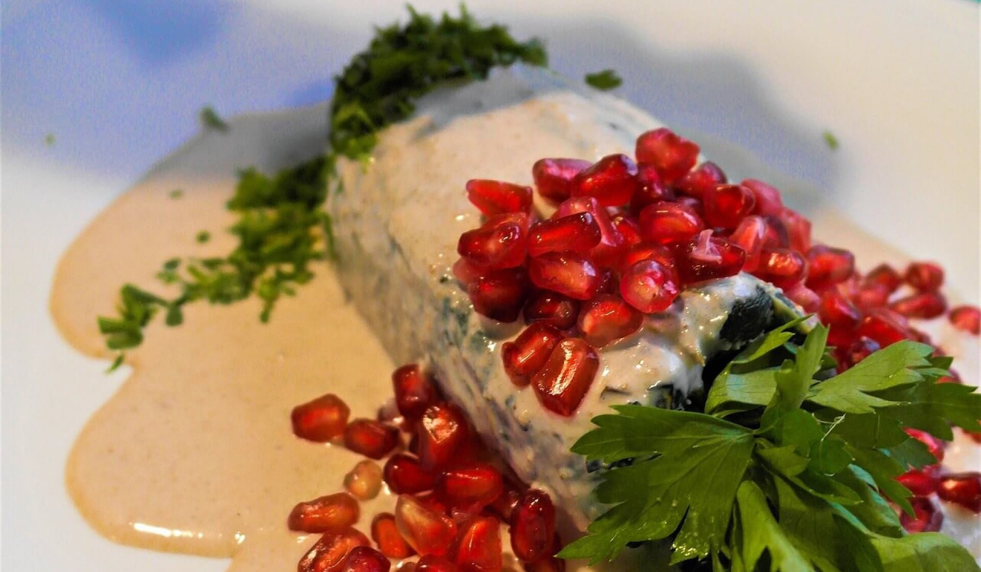 Mexican chiles en nogada on a plate with colorful green cilantro, red pomegranate seeds, and white sauce