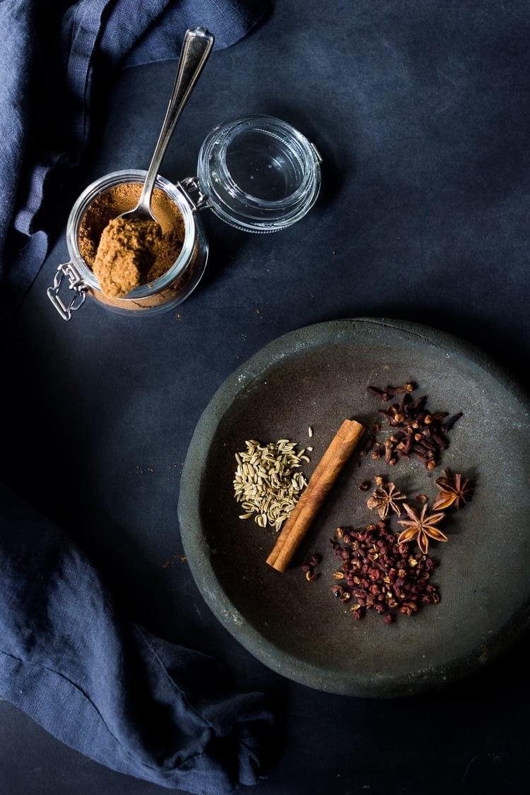 jar with Chinese Five spice with spoon, beside small dish with whole spices - fennel seeds, star anise, cinnamon stick, cloves, and Szechuan peppercorns