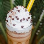 Starbucks Frappuccino with whipped cream and caramel drizzle, logo visible on cup, cafe interior setting