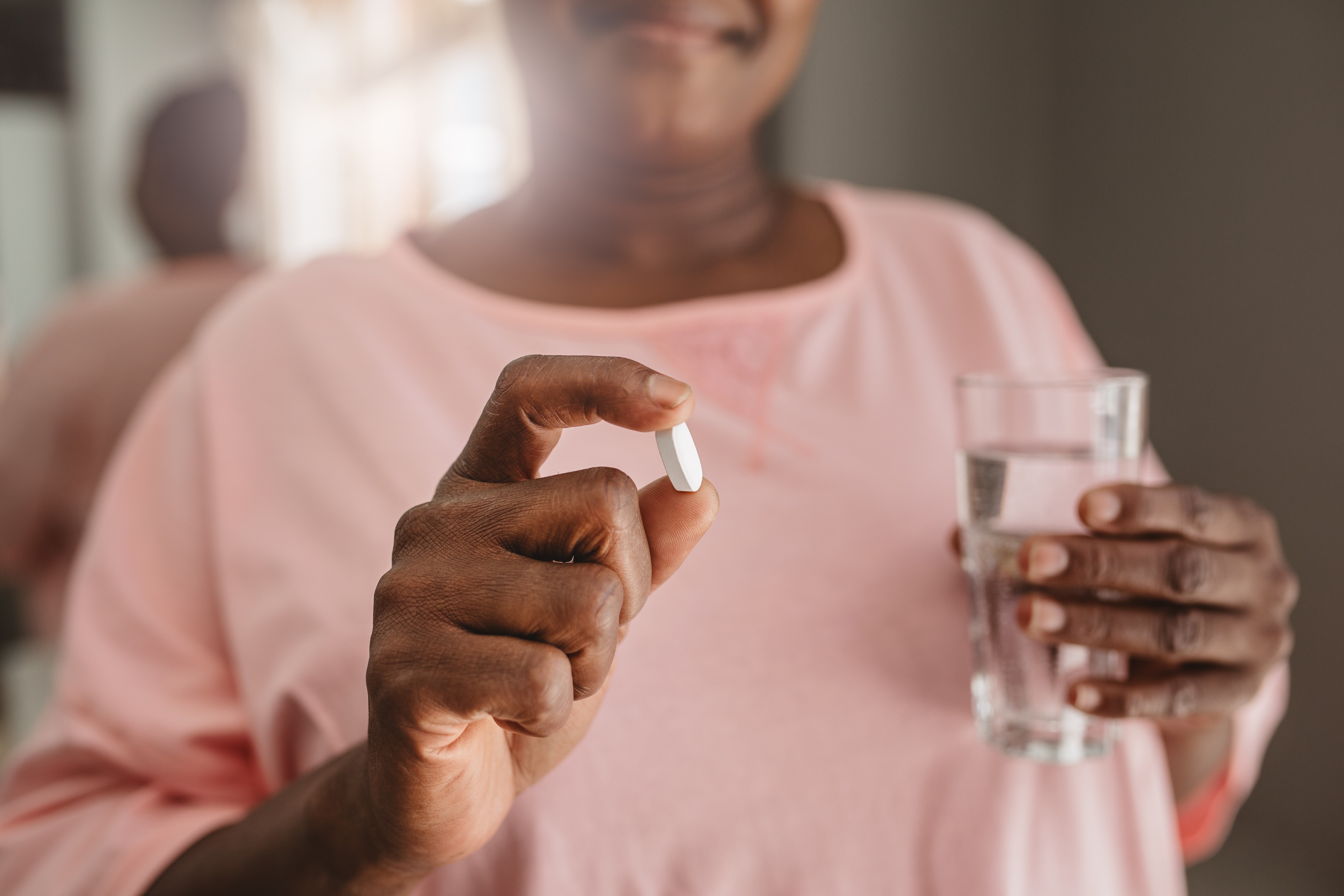 A mature woman holding a white pill and a glass of water.