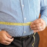 Man measuring his waist with a tape measure indicating healthy body fat level