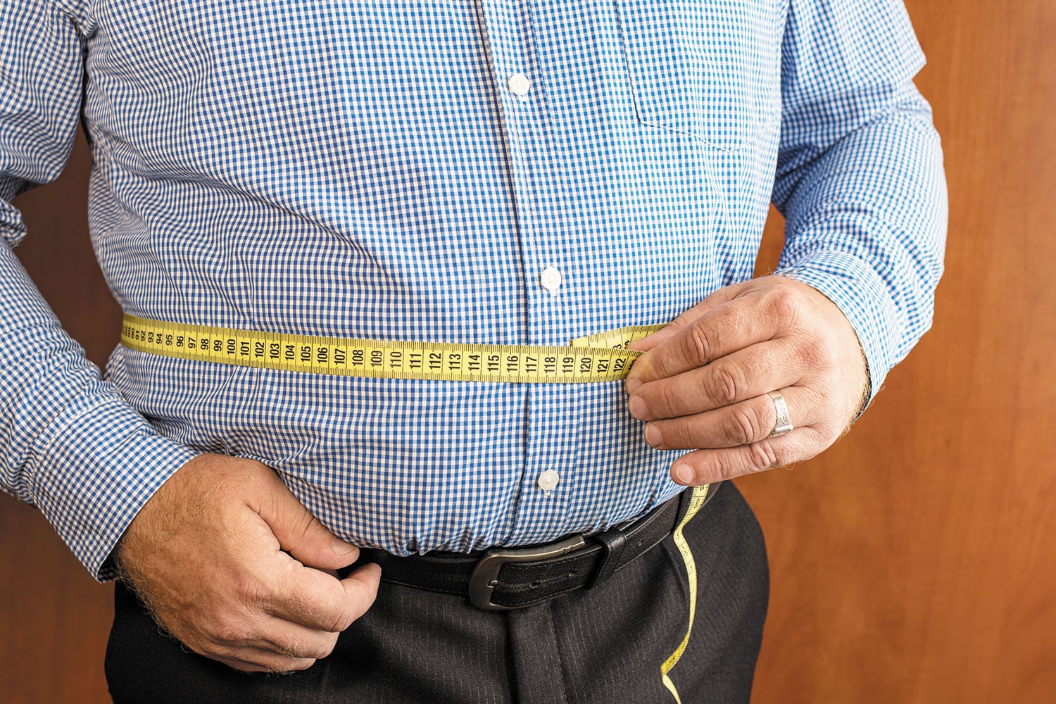 Man measuring his waist with a tape measure indicating healthy body fat level