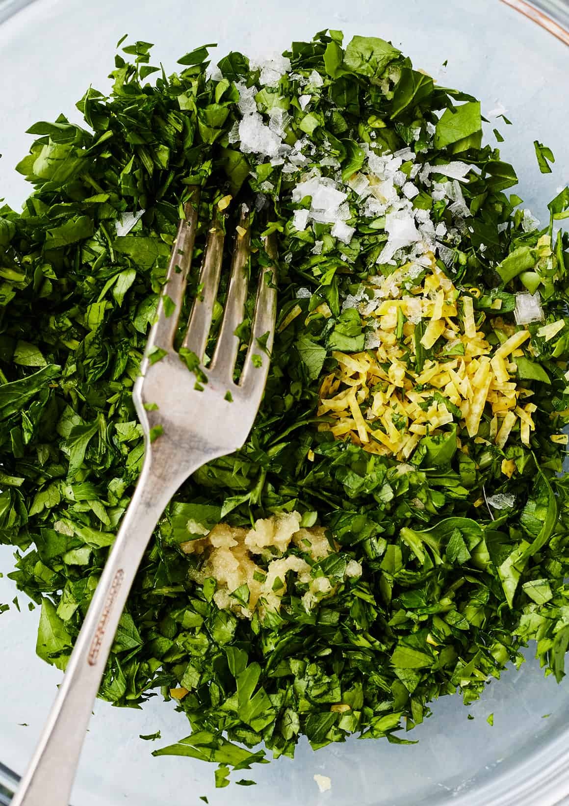 Chopped parsley, lemon zest, garlic, and salt in glass bowl with fork