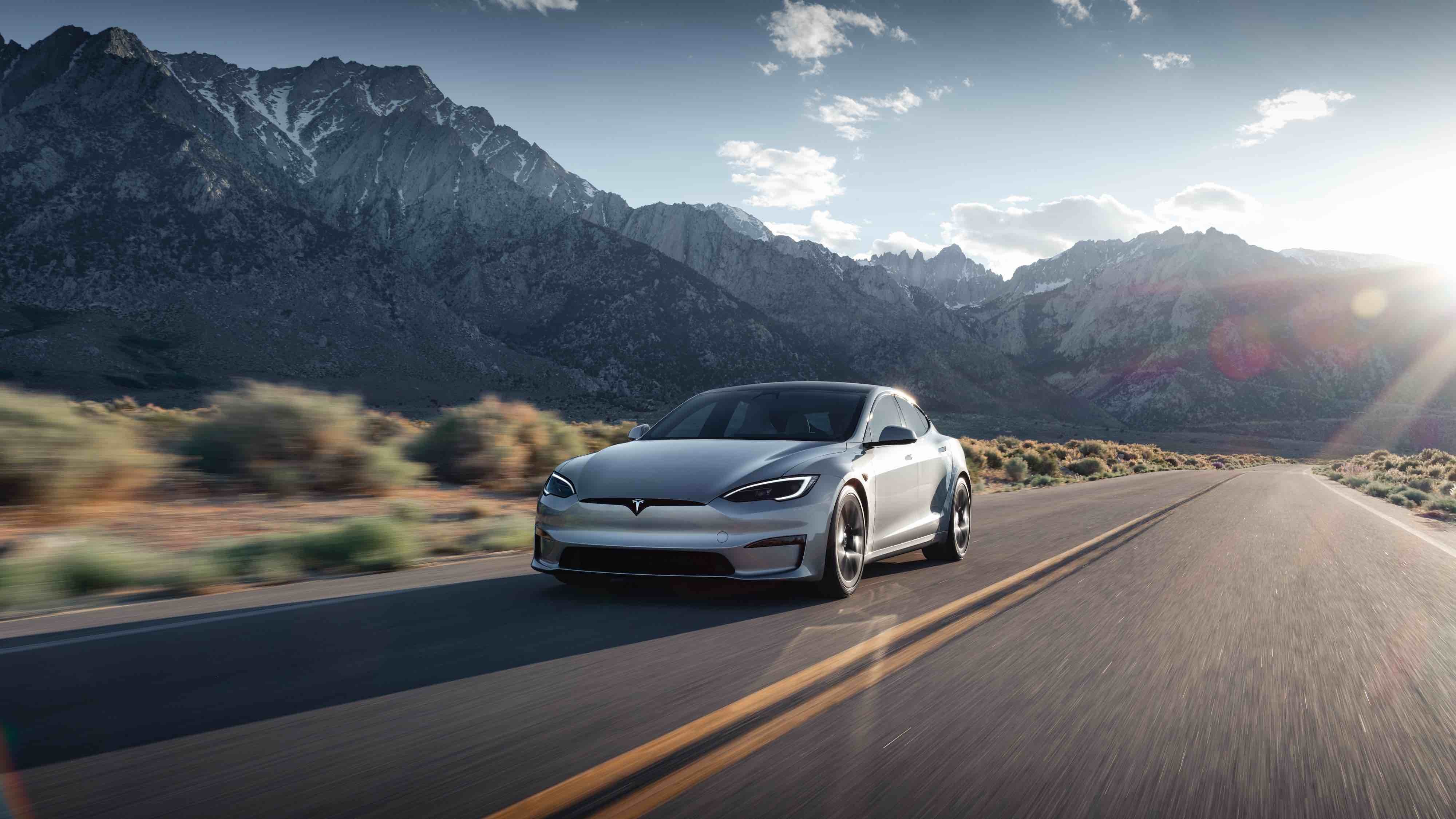 A silver Tesla Model S driving along a highway next to a mountain