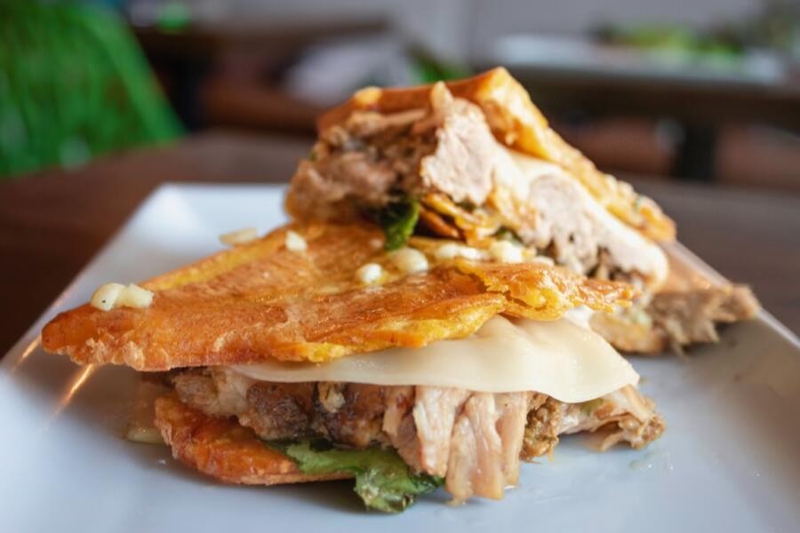 A jibarito de lechon, showcasing fried plantains, pork, lettuce, and mayo