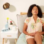 Woman using a diffuser on her bed, promoting wellness through aromatherapy