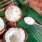 Fractionated coconut oil in a clear glass bottle next to a fresh coconut.
