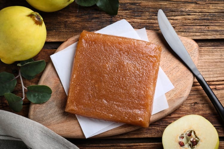 Quince paste served on a wooden board alongside fresh quince fruits