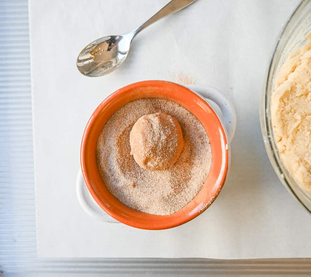 Snickerdoodle cookie dough being rolled into a cinnamon-sugar mixture before baking.